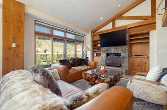 The living room in Peaks Penthouse 617 features large windows with a view of the mountains, a fireplace, and comfortable leather and fur-covered seating.