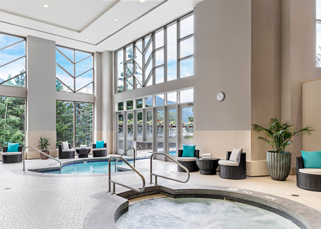 An expansive indoor hot tub area at The Westin Deluxe Studio Suite features multiple hot tubs, comfortable seating, and large windows offering views of the surrounding natural landscape.