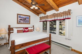 A cozy bedroom inside Crestwood 1212 featuring a wooden king bed, red accents, and a large window with an outdoor view.
