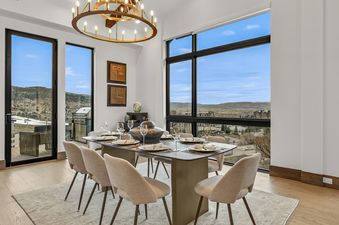 The dining area at Nocturne View, showcasing a modern dining table set for eight, with large windows offering expansive views of the mountains and a town.