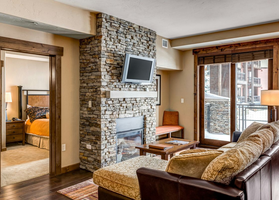 A cozy living area at Trailhead Lodge 2105 features a fireplace, comfortable seating, and a large glass door opening to a snowy exterior view.
