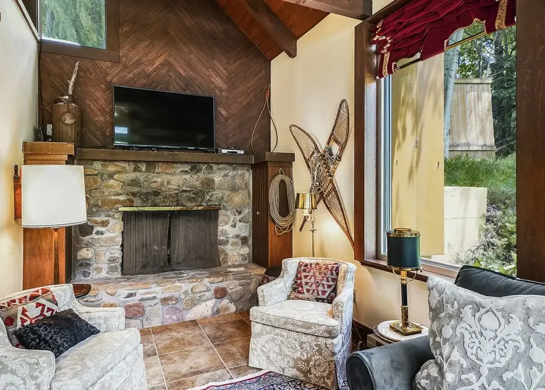 A cozy lounge area in Summer Haus with a stone fireplace, two armchairs, a television, and decorative snowshoes.