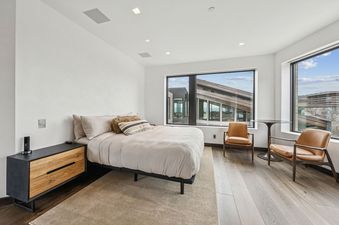 The bedroom at Mountainhead features a comfortable bed with light-colored bedding and pillows, a modern nightstand, and large windows offering an exterior view.