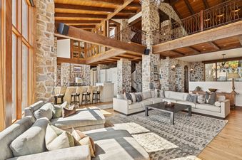 The great room of Snow Pine Lodge at Deer Valley, featuring two large sectional sofas, a dark wood coffee table, a bar area, and rustic stone and wood beam architecture.