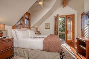 A bedroom with a bed, nightstand, and a view of trees through a French door.