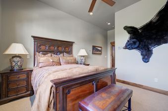 A cozy bedroom with a large wooden bed, matching nightstands, decorative lamps, and a bear rug adorning one wall.
