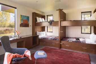 Bunk bedroom at Wilderness Meadow with built-in wooden bunk beds, a red rug, and large windows looking out to nature.