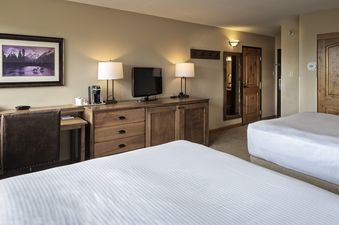 A hotel room at Beaver Run Resort with two beds, a wooden desk and chair, a flat-screen TV, a coffee maker, and two lamps.