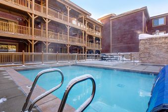 The photo shows the inviting pool and hot tub area at Black Bear 207, surrounded by snow-dusted railings and buildings.