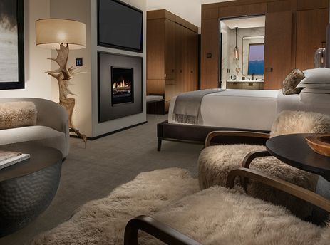 A luxurious bedroom and lounge area featuring a fireplace, plush seating, and elegant decor, with a glimpse of the bathroom beyond.