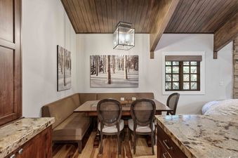 A cozy dining nook with a built-in banquette and a wooden table, adorned with nature-inspired artwork and illuminated by a lantern chandelier.