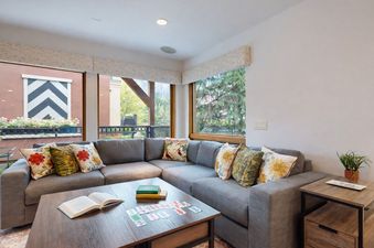 Upstairs Den in Montaneros 222 featuring a comfortable grey sectional, wooden coffee table with a card game, and large windows with outdoor views.