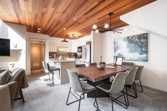 Dining table and kitchen area at Foxglove 1 featuring a wood ceiling and modern decor.