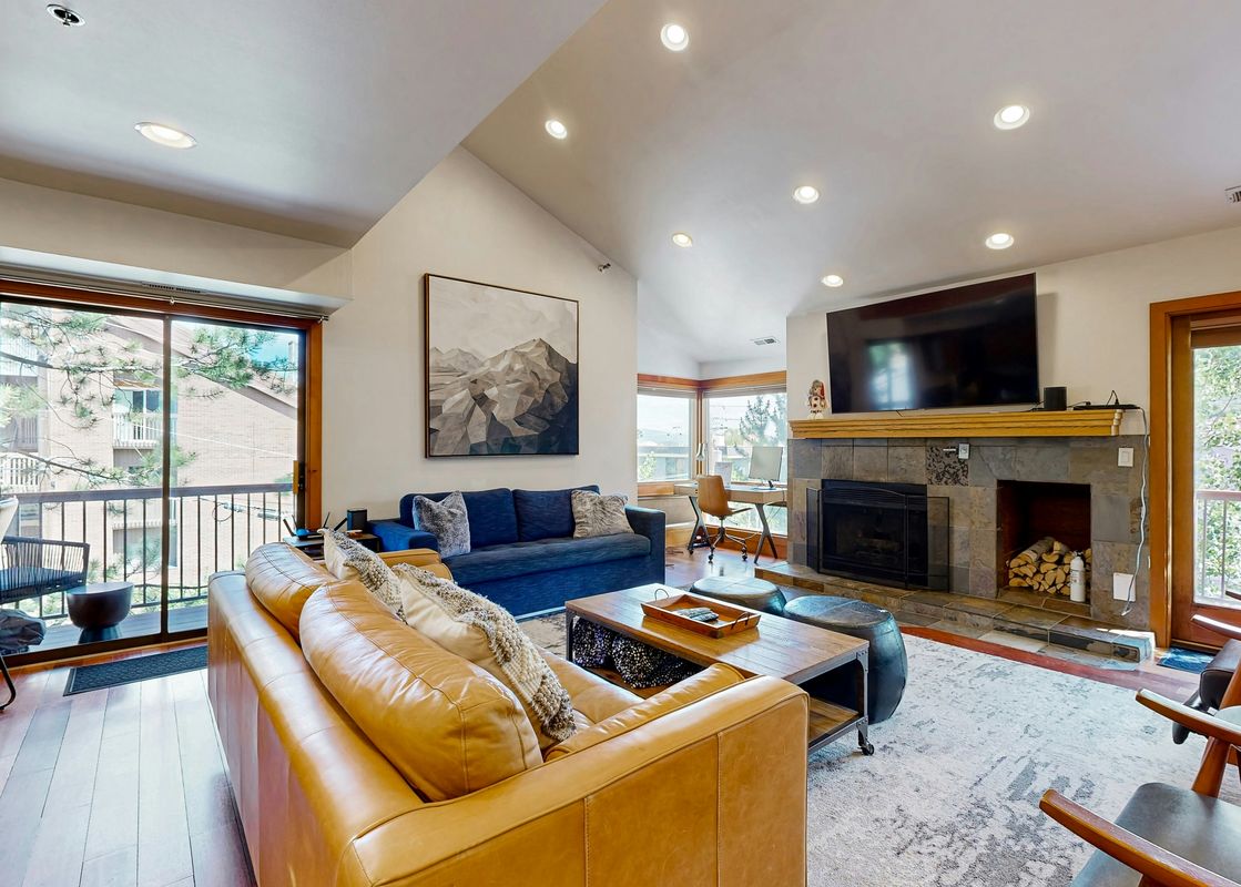 The living area features a brown leather sofa, a blue sofa, a fireplace, and a large flat-screen TV.