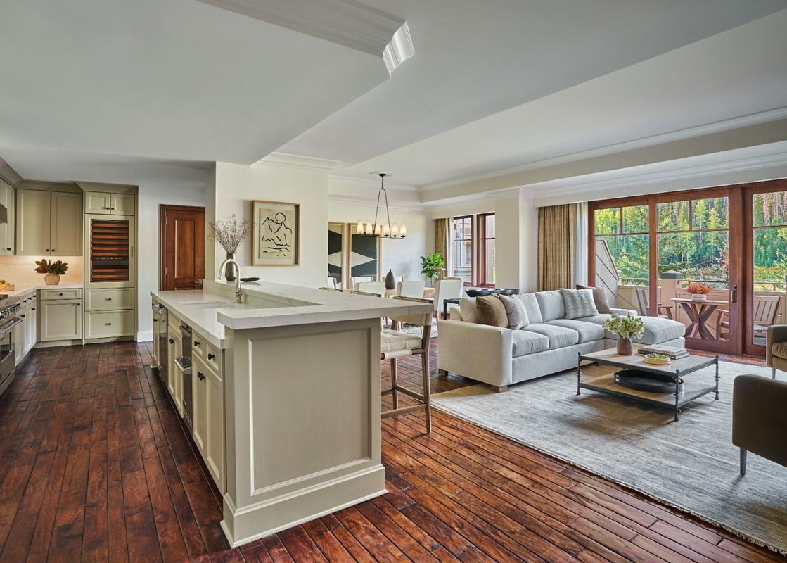 A spacious and elegant open-concept living area with a full kitchen, dining space, and a comfortable living room, all featuring rich hardwood floors and access to a private balcony with a lush resort view.