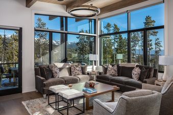 Moonlight Basin 9 Deep Forest Drive living room features a large sectional sofa, two armchairs, and a coffee table. The living room has floor-to-ceiling windows that offer a stunning view of the mountains.