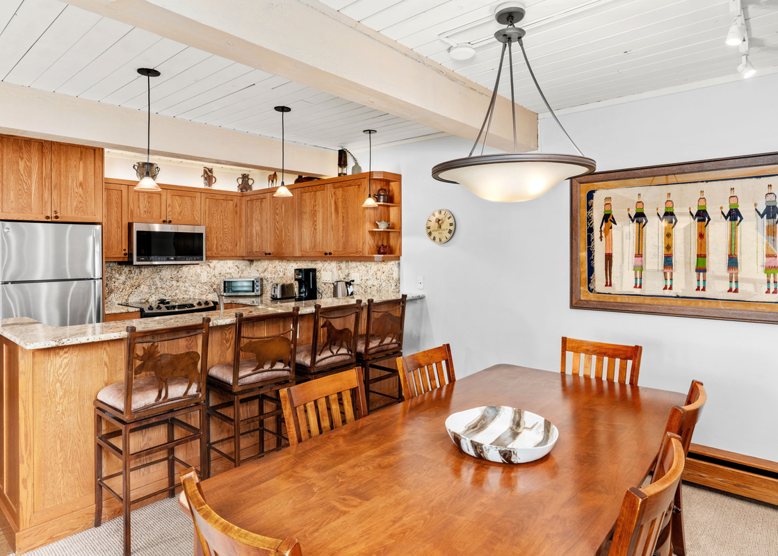 The kitchen and dining area at Top of the Village Leaf 401, featuring a wooden dining table, a kitchen with wooden cabinetry, stainless steel appliances, and unique animal-themed bar stools.