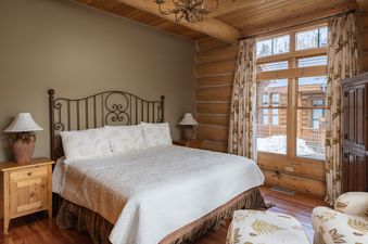 The inviting bedroom at Wild Bear Haven features a comfortable bed, rustic log walls, and plenty of natural light.