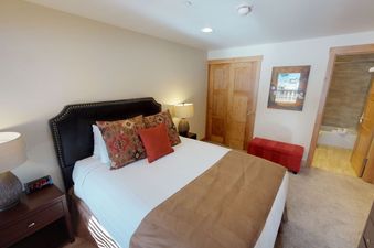 The bedroom in Manor Vail 121 features a plush king bed with a brown blanket, a bedside table with a clock, and two side tables with lamps.