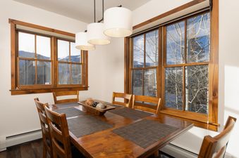 The dining area at Aspen Trail Junction features a wooden table, chairs, and large windows with views of the snow-covered outdoors.