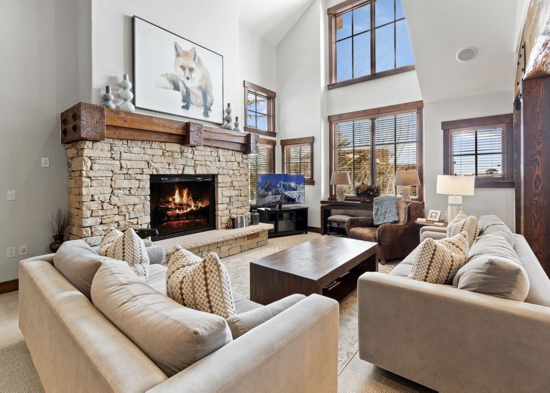 A spacious and brightly lit living room in Silver Star 33 featuring a large stone fireplace, comfortable sofas, and tall windows.