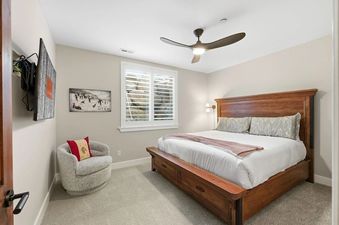 A modern bedroom with a large wooden king bed, accent chair, and shuttered window at Snowline at Black Rock Ridge.