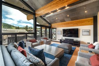 Royal Plaza Penthouse offers a modern living room with multiple sofas and a large screen TV, while enjoying panoramic views of the mountain peaks and valley.