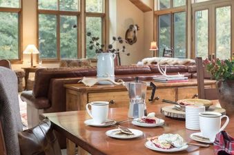 A dining table set for coffee and dessert in a rustic living area with large floor-to-ceiling windows at Teton Grove.