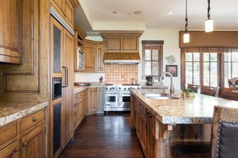 A rustic-chic kitchen featuring rich wood cabinetry, granite countertops, and stainless steel appliances, with an island and bar stools.