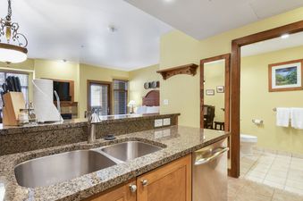 The Sundial Lodge Studio's kitchen features granite countertops, a double sink, and a dishwasher, with a view into the living area, bedroom, and an adjacent bathroom.