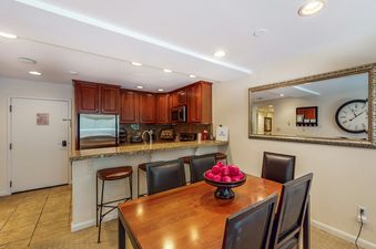 The dining room in Fallridge 302 features a wooden table with chairs, a bowl of apples, and a mirror reflecting the hallway and kitchen.