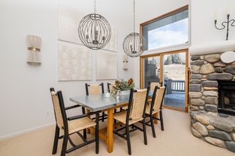 A dining room with a large window looking out to a snow-covered mountain landscape, a fireplace, and a wooden table with chairs.