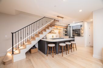 A modern entertainment space in the Powder Day Chalet with a kitchenette, bar, and open staircase with illuminated steps.