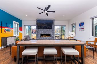The living area at Apres Chalet Winter Park features a stylish fireplace and a large television, complemented by comfortable seating and a bar-height table with stools.
