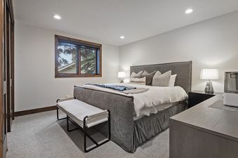 The bedroom at Antlers Estate features a large bed with a grey upholstered frame and headboard, light bedding, and an assortment of decorative pillows, accompanied by bedside tables and lamps.