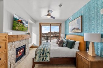 A cozy bedroom at Edgemont 2401 featuring a comfortable bed, fireplace, and a large window with mountain views.