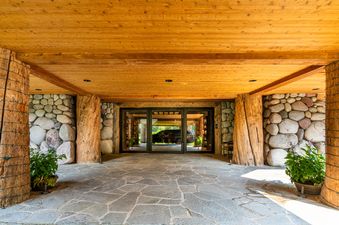 The grand entrance of Northstar Chalet, featuring a stone path, large wooden pillars, river stone walls, and glass doors leading into the interior.