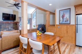 An open-concept living and dining area in Krystal Villa 5, featuring a wooden dining table, leather sofa, stone fireplace, and flat-screen TV.
