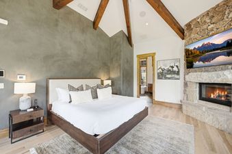 Master bedroom at Northside Retreat with a king bed, vaulted beamed ceiling, and a stone fireplace.