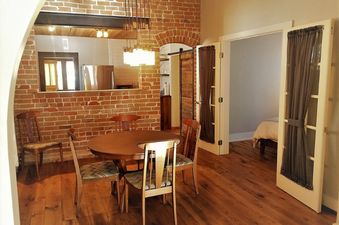A dining area with a table and chairs. The dining area is located next to a kitchen area and has a brick wall.