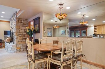 A cozy dining area at The Charter G0505 featuring a round wooden table, six light-colored wooden chairs with plaid cushions, and two ornate chandeliers.