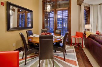 The dining area at Silver Star 702 features a round wooden table, stylish chairs, and a large mirror reflecting the light from the windows.