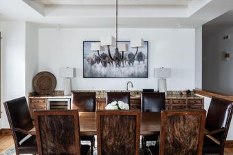 The dining table of Moonlight Basin Luxury Suite 6A is set with brown leather chairs, and there are wooden cabinets and a wine fridge in the background.