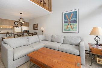 The living area of Meadow Ridge 31 features a large sectional sofa, a wooden coffee table, and a unique ski-themed wall art, with the kitchen and dining area visible in the background.