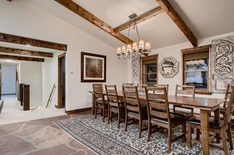 The dining room at the Lodge at Ski Hill features a large wooden table with eight chairs, a chandelier, and exposed wooden beams.