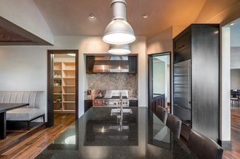 A modern kitchen with a dark granite island, stainless steel appliances, and industrial pendant lighting.