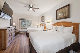 A cozy bedroom with two queen beds, a wall-mounted TV, a dresser, and a window offering an outdoor view.