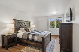 The cozy bedroom at Sweet Peaks, showcasing a rustic wooden bed with plaid bedding, nightstands, a dresser, and a window with a view of a ski lift.