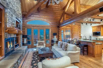 The spacious living area within Tristant 125 features a grand stone fireplace, comfortable sofas, and large windows with outdoor views.