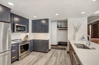 A modern kitchen with stainless steel appliances, dark cabinets, white countertops, and a large sink with a chrome faucet.